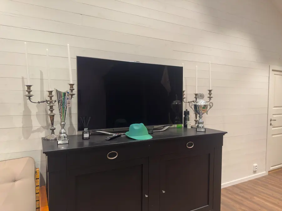 Silverpokaler och kandelabrar på en mörk byrå under en tv.